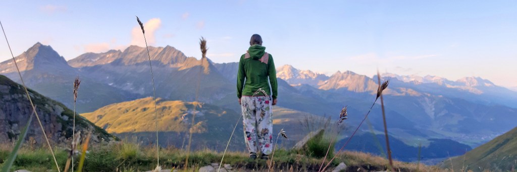 Die Ergotherapeutin Katja Hausmann steht vor einer Bergkette in den Schweizer Alpen. Im Tal fließt der junge Rhein.